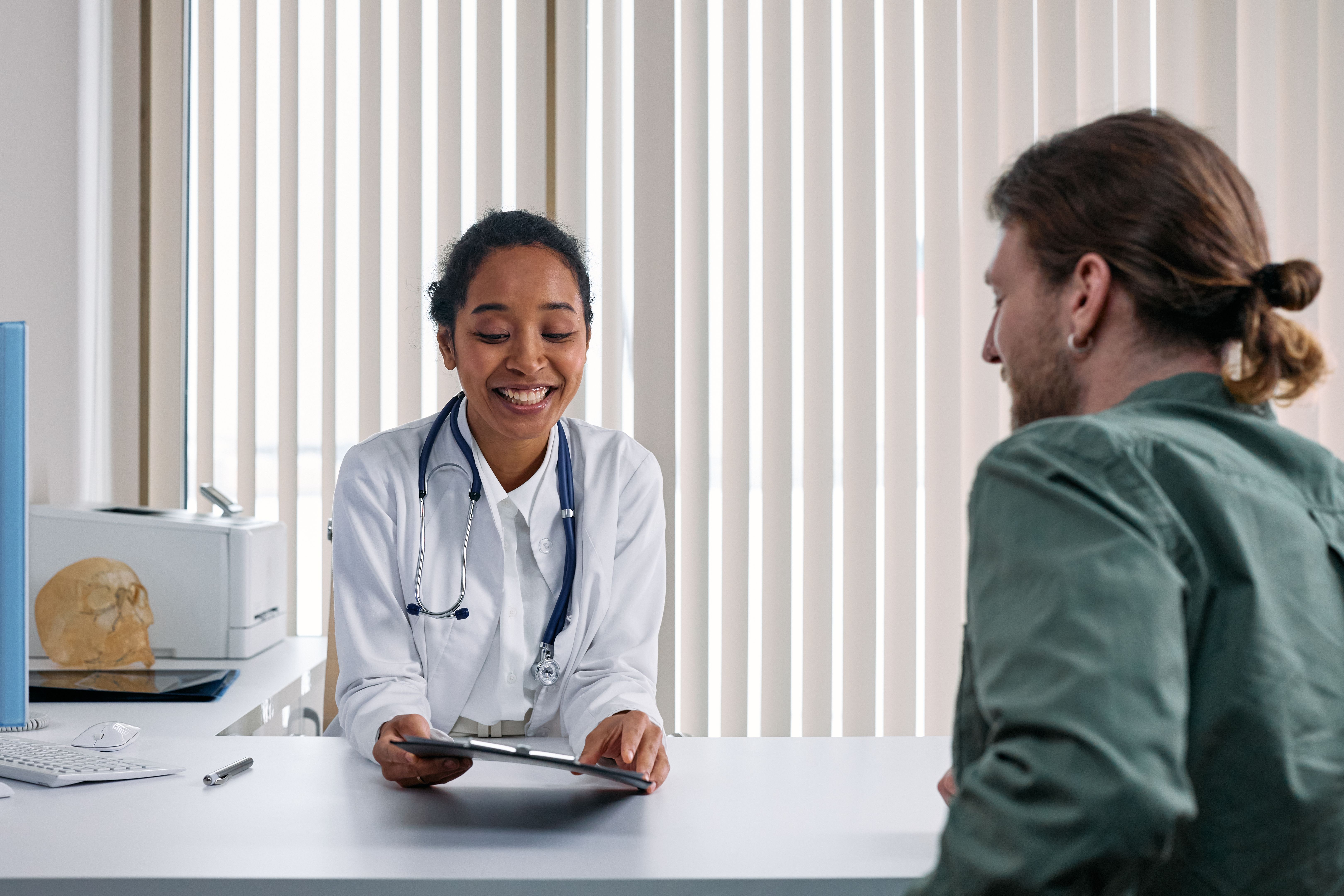 Doctor holding a tablet while talking with a patient, reviewing an AI-generated draft note for accuracy